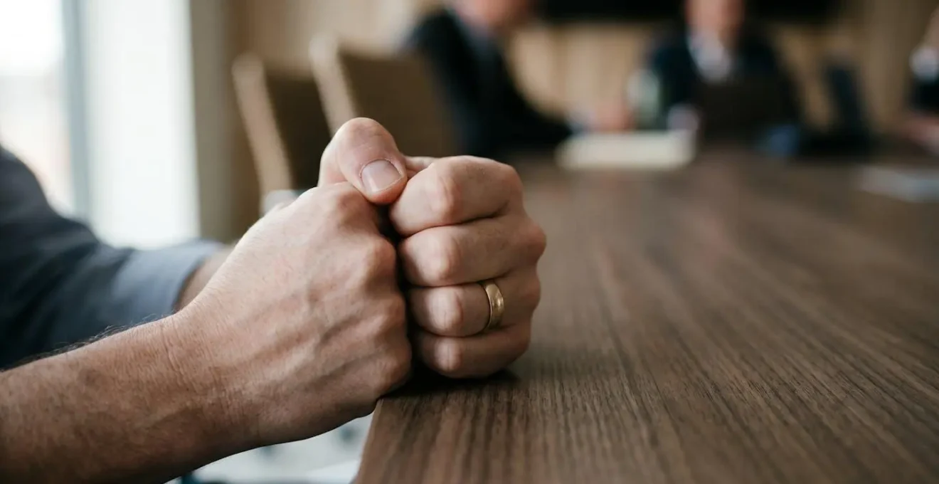 Gros plan sur les mains croisées d'une personne lors d'une réunion silencieuse traduisant l'inconfort psychologique